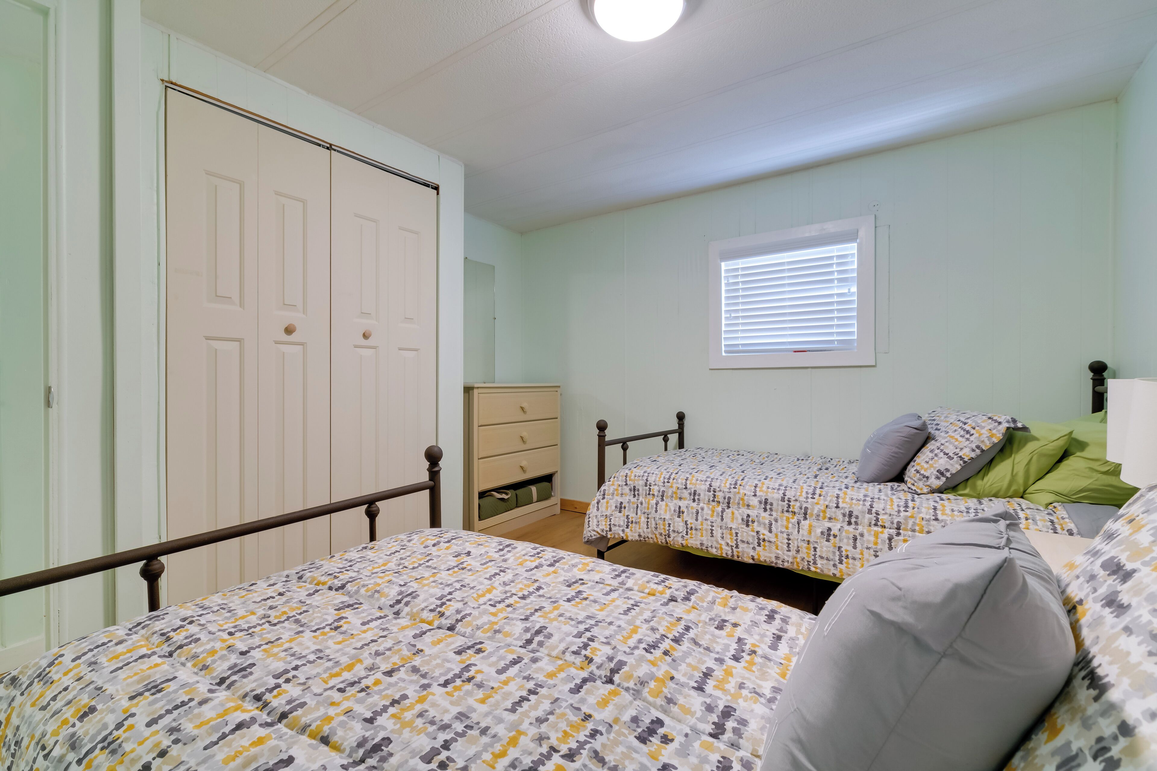 A bedroom with two beds, a dresser, and a window with blinds.