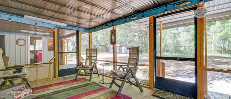 A wooden deck with a colorful striped rug, wooden chairs, and a table.