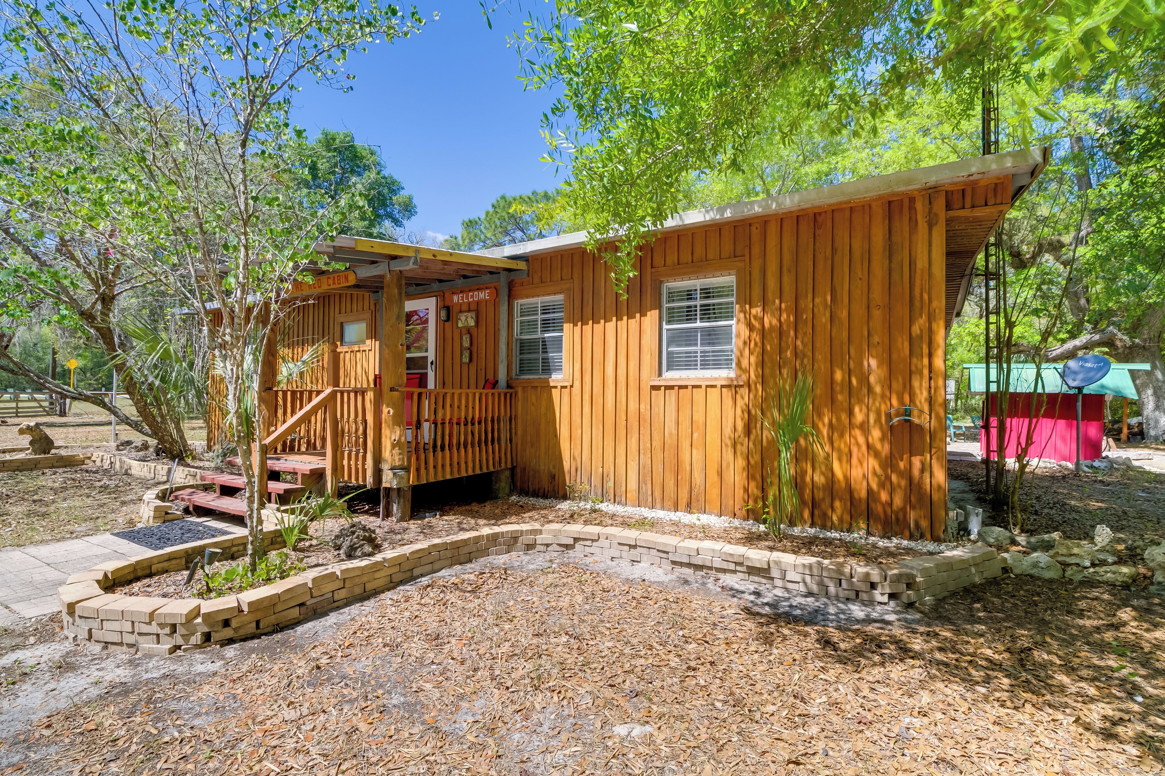 A wooden cabin with a 'Welcome' sign, a covered porch, and a brick garden bed.