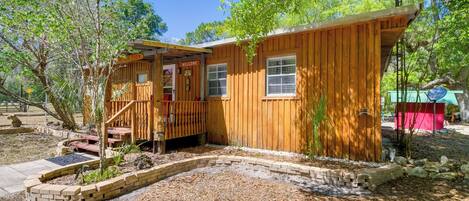 A wooden cabin with a 'Welcome' sign, a covered porch, and a brick garden bed.