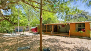 Une cabane en bois avec une véranda, une balançoire et un bâtiment rouge en arrière-plan.