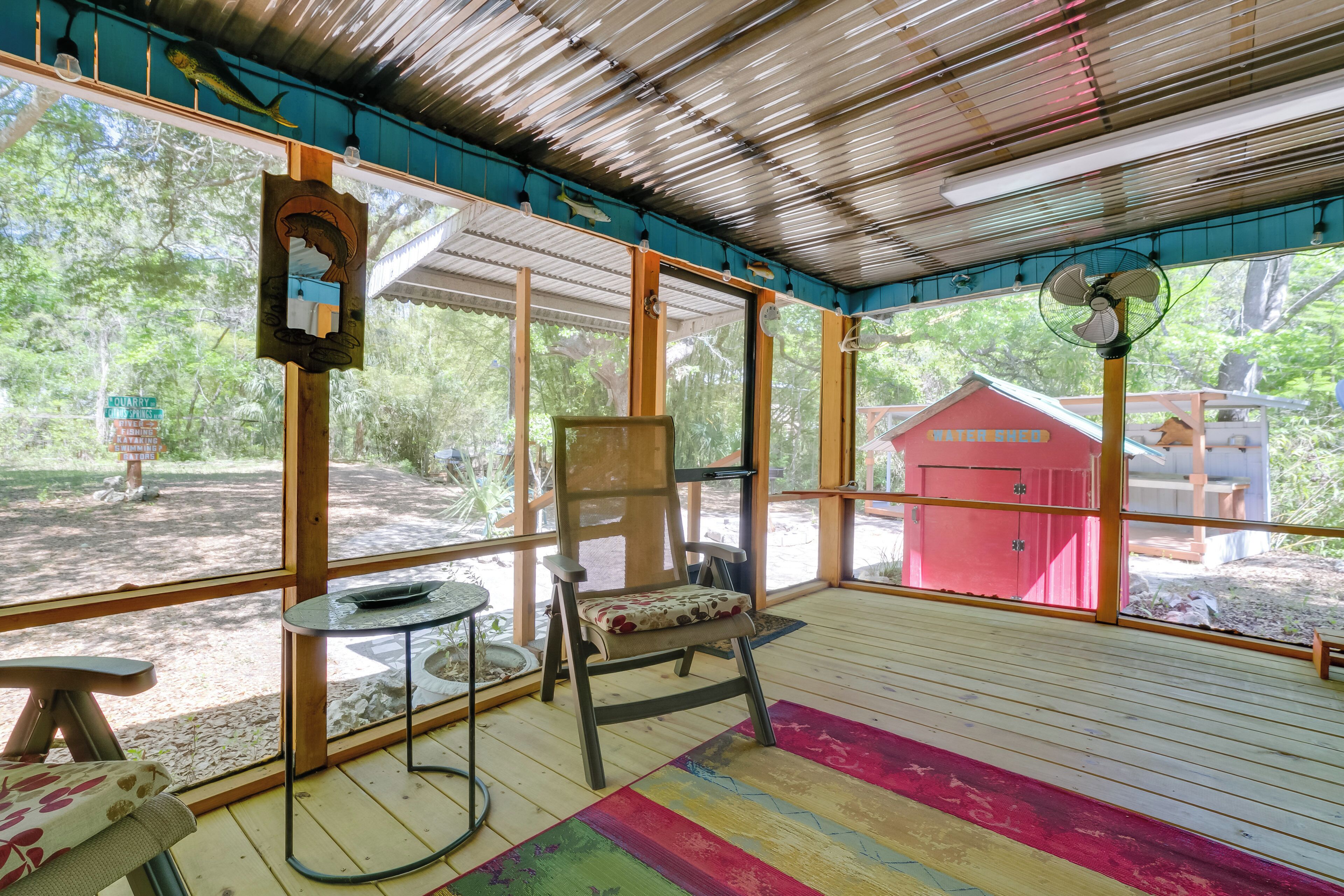 A covered outdoor seating area with a chair, table, and a red shed in the background.