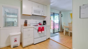 Une cuisine de taille réduite, avec des meubles blancs, un four à micro-ondes, une cuisinière et une poubelle.