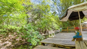 Un pont en bois, situé dans une zone boisée, avec un banc et un espace de repos abrité.