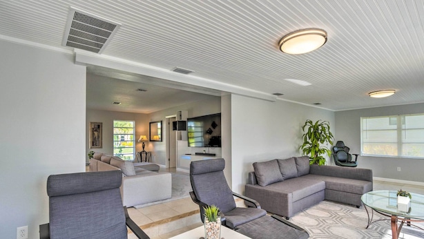 A modern living room with grey sofas, a glass coffee table, and a white side table. There is a kitchen area in the background with a TV and a plant. - Punta Gorda Escape w/ Private Lanai & Pool! (Punta Gorda)