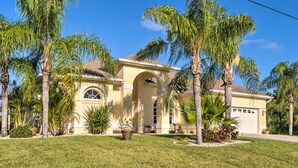 A two-story house with a large arched entrance, surrounded by palm trees and a well-maintained lawn. - Port Charlotte Home on Canal w/ Lanai & Pool! (Port Charlotte)