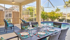An outdoor dining area with a pool, wicker furniture, and a view of palm trees. - Port Charlotte Home on Canal w/ Lanai & Pool! (Port Charlotte)