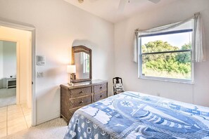 Une chambre à coucher comprenant un lit, une commode, un miroir et une fenêtre donnant sur un paysage verdoyant.