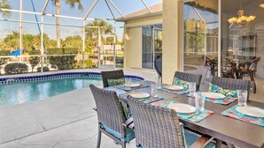 An outdoor dining area with a pool, wicker chairs, and a glass-enclosed patio. - Port Charlotte Home on Canal w/ Lanai & Pool! (Port Charlotte)