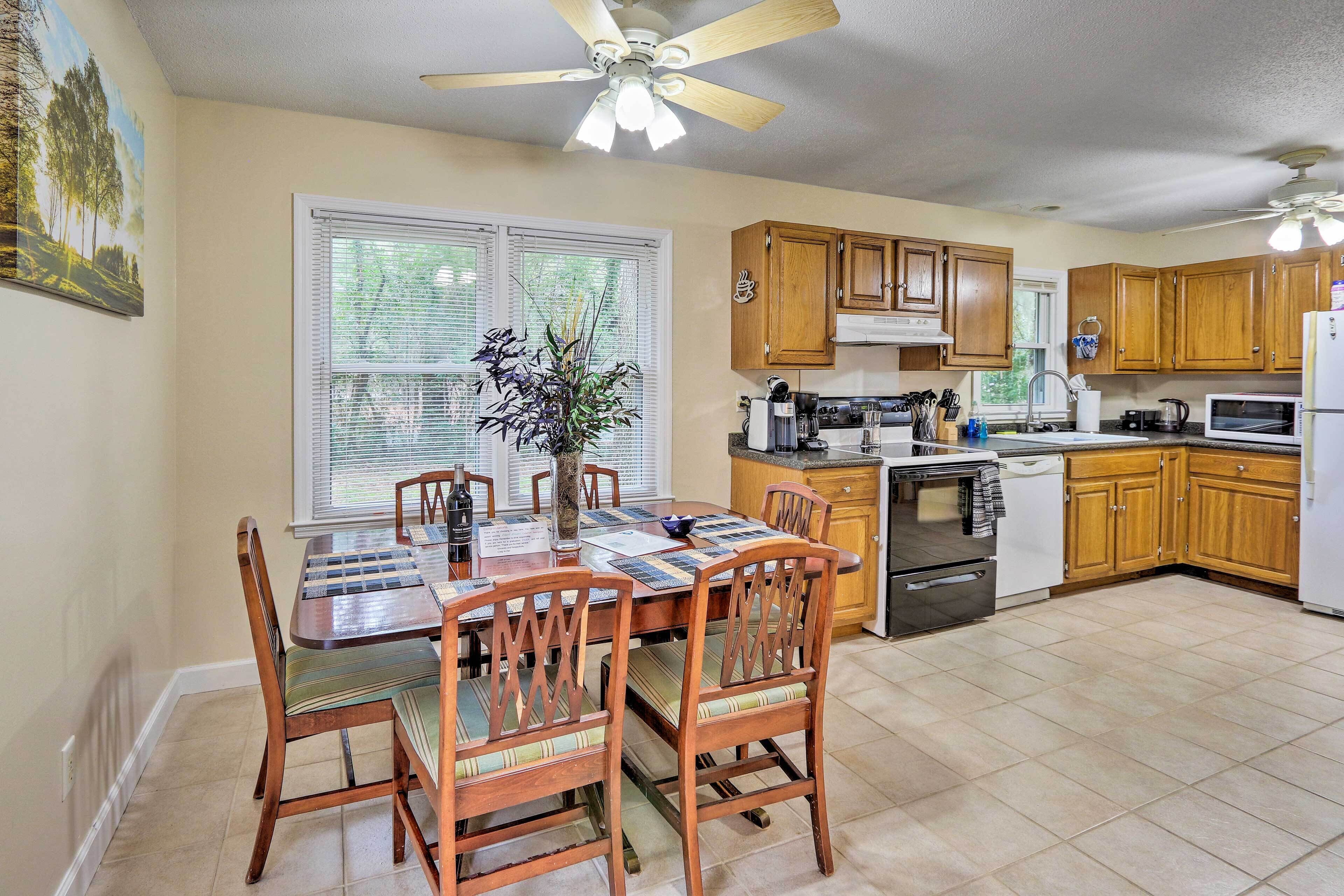 A kitchen with wooden cabinets, a dining table with chairs, a ceiling fan, and a window with blinds.