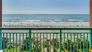 A beach view from a balcony with a railing, palm trees, and a clear sky. - Myrtle Beach Oceanfront Condo w/ Pool & Lazy River (Myrtle Beach)