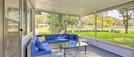 Une terrasse couverte avec un canapé d’angle bleu, une table basse en verre et un tapis à motifs.
