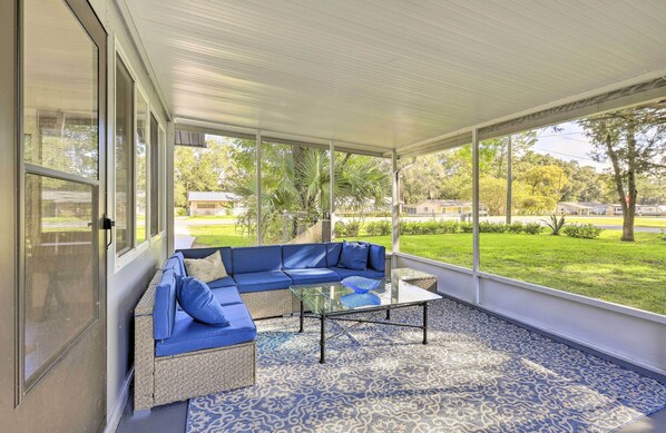 Een overdekt terras met een blauwe modulaire bank, een glazen salontafel en een kamerkleed met dessin.