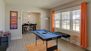 Een kamer met een pooltafel, een eethoek en een groot raam met oranje gordijnen.