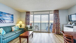 Une pièce comprenant un canapé, une table, une chaise, un téléviseur et un balcon avec des rideaux.