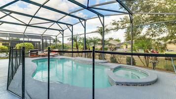 A covered outdoor swimming pool with a metal frame and mesh sides, surrounded by a fence.