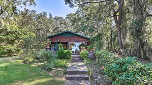 A rustic cabin with a stone pathway leading to the entrance, surrounded by lush greenery and trees. - Rustic Beaufort Home w/ Stunning Marsh Views! (Beaufort)