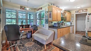 A kitchen with wooden cabinets, a granite countertop, and a dining area with a chair and a rug. - Rustic Beaufort Home w/ Stunning Marsh Views! (Beaufort)