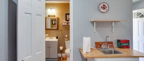 A kitchen with a wooden countertop, a sink, and a wall-mounted shelf.