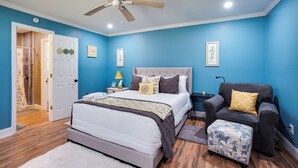 A bedroom with a bed, a chair, a footstool, a ceiling fan, and a door. - Saint Helena Island Getaway w/ Marsh Views! (Saint Helena Island)
