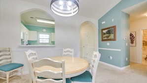 A dining area with a round table and chairs, a mirror above the table, and a light fixture above.