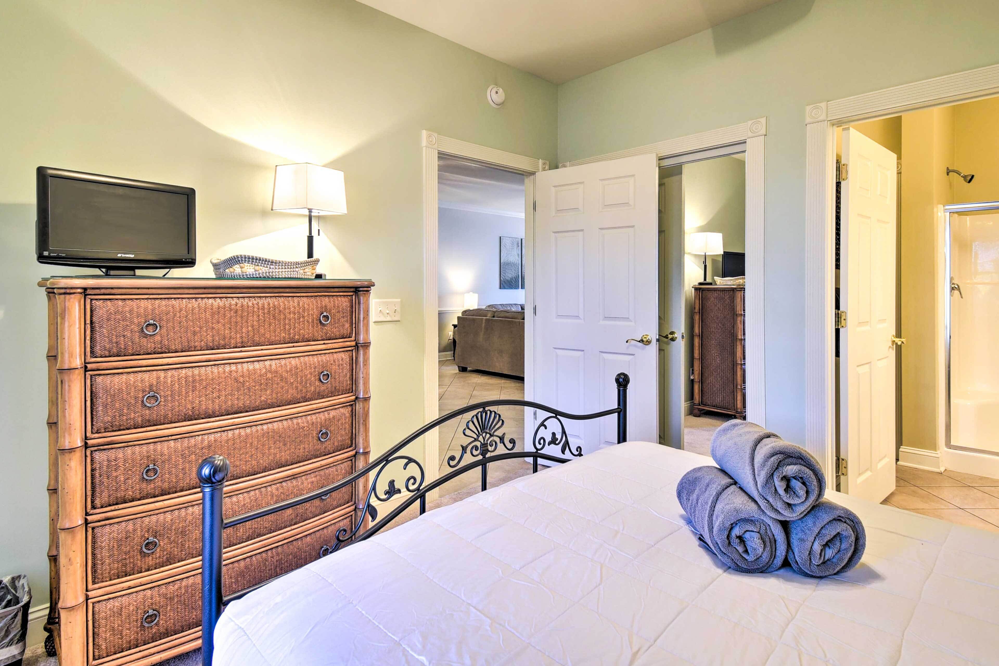 A bedroom with a bed, a dresser, a television, and a door leading to another room.