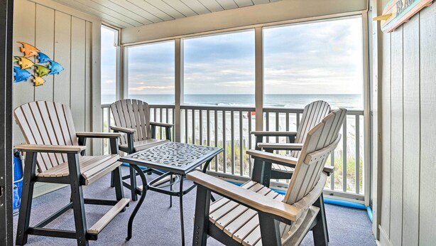 Uma área de estar coberta ao ar livre com cadeiras Adirondack e uma mesa de metal, com vista para o oceano.