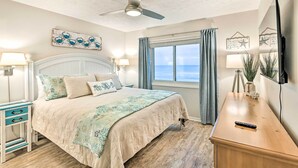 Quarto com cama, ventilador de teto, janela com cortinas e mesa de cabeceira com abajur.