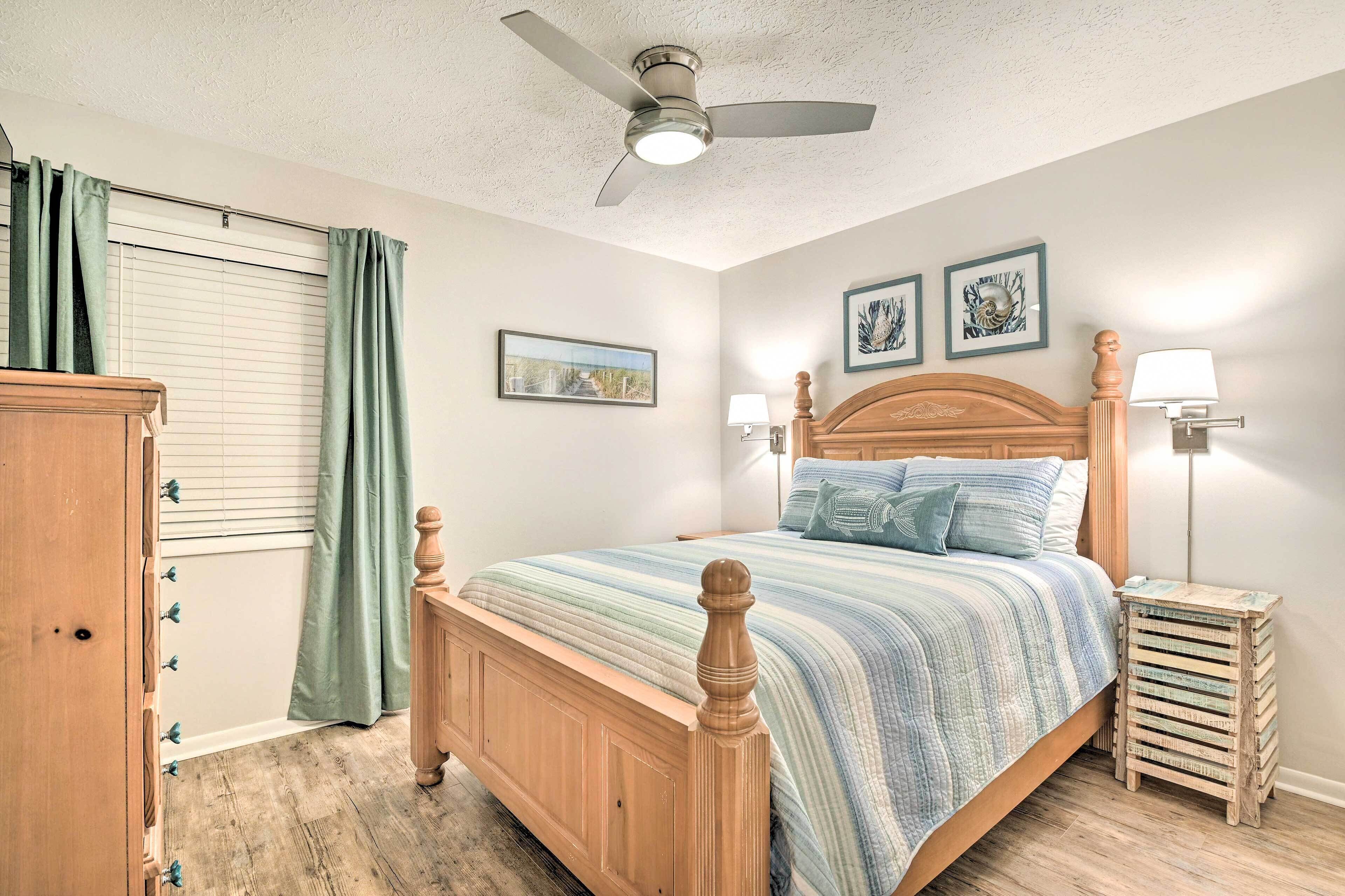 A bedroom with a wooden bed, a ceiling fan, a nightstand with a lamp, and a window with curtains.
