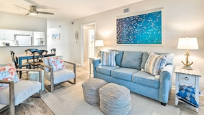 Uma sala de estar com um sofá azul, pufes combinando e uma área de jantar com mesa e cadeiras de madeira.