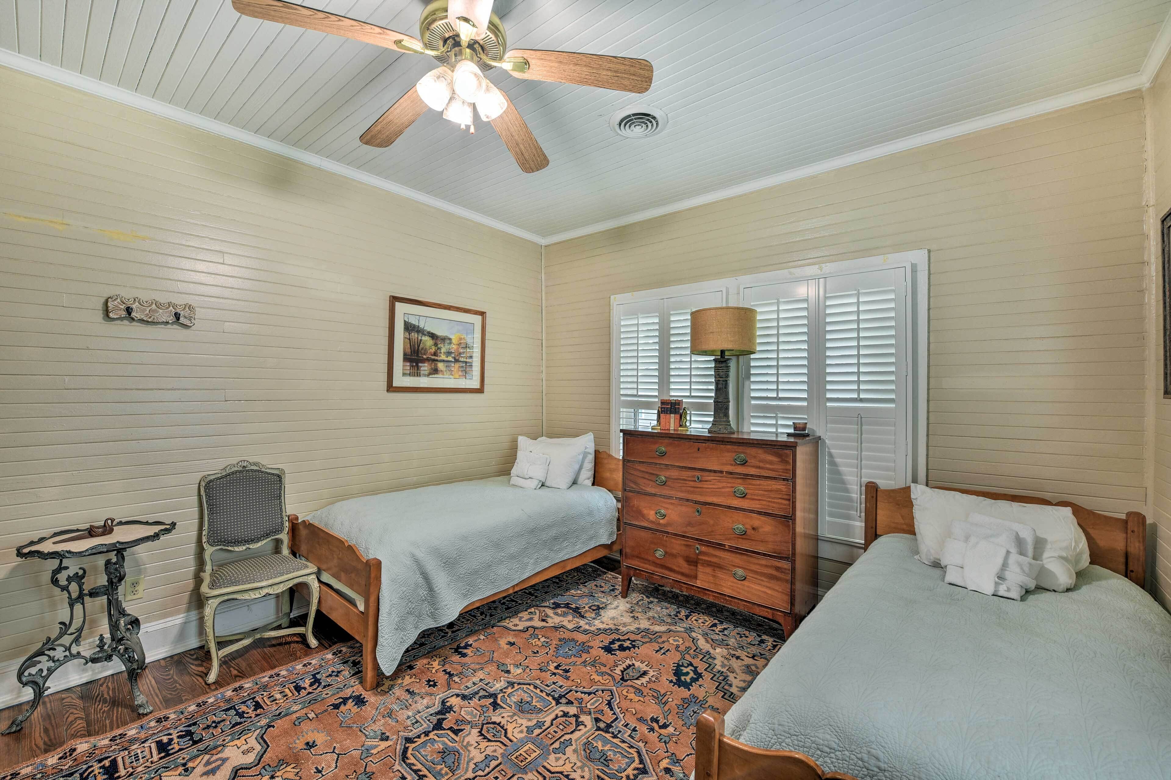 A bedroom with two single beds, a wooden dresser, a chair, a table, and a ceiling fan.