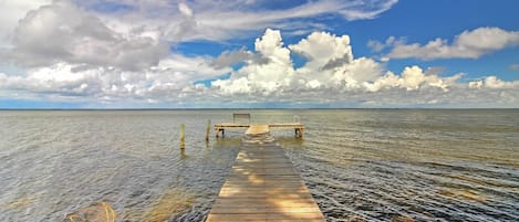 A wooden pier extending into calm water, with a bench at the end.