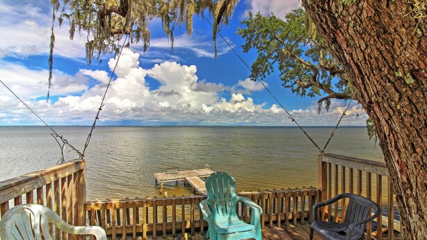 A wooden deck with chairs overlooking a calm body of water, a dock, and a tree with hanging moss. - Santa Rosa Beach Bungalow 5 Mi to the Gulf Shore! (Santa Rosa Beach)