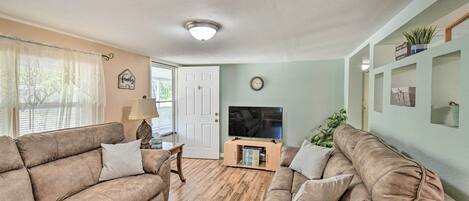 A living room with two brown sofas, a wooden coffee table, a TV on a stand, and a door leading outside.
