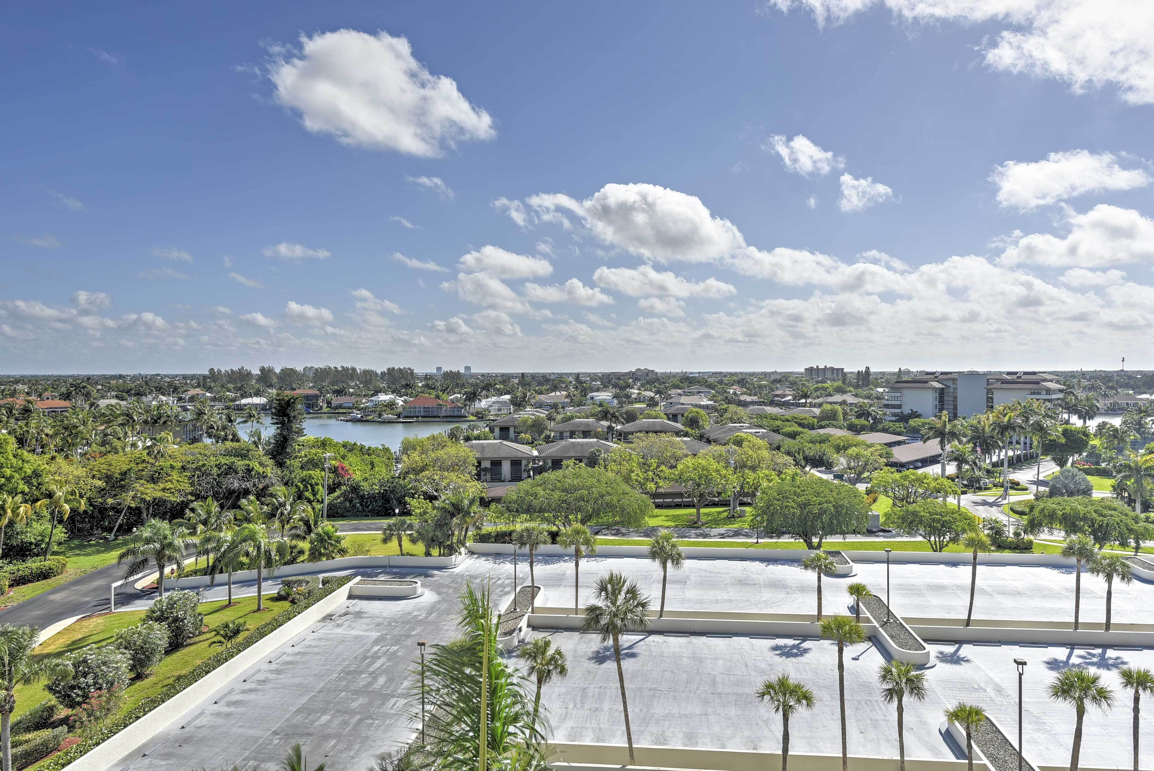 A large parking area with palm trees, a lake, and buildings in the background.
