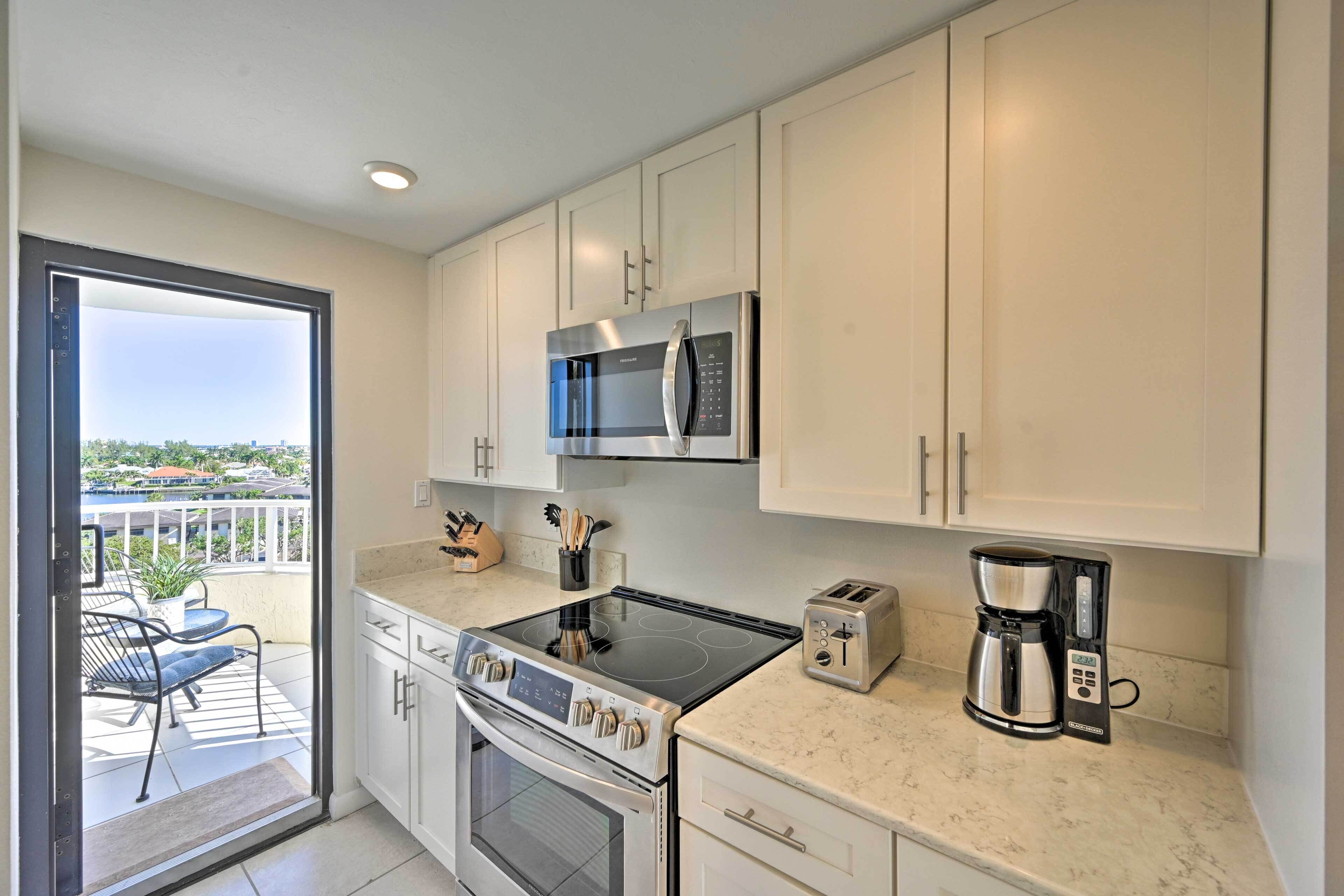 A modern kitchen with stainless steel appliances, a large window, and a balcony with outdoor furniture.