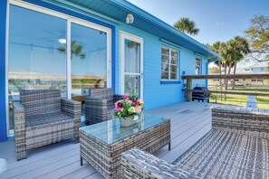 A blue house with a covered patio area featuring wicker furniture and a glass-top table with a flower arrangement.