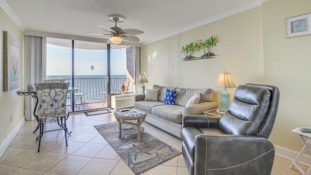 A living room with a balcony, a ceiling fan, a sofa, a leather chair, a coffee table, and a small side table. - Oceanfront Resort-style Condo in Myrtle Beach! (Myrtle Beach)
