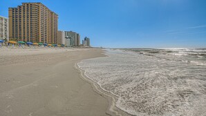 A beach with a row of beach umbrellas and a tall hotel building. - Oceanfront Resort-style Condo in Myrtle Beach! (Myrtle Beach)
