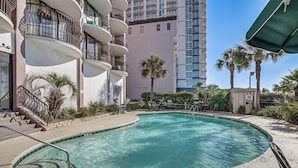 A swimming pool with a curved edge, surrounded by a concrete deck and a metal railing. - Oceanfront Resort-style Condo in Myrtle Beach! (Myrtle Beach)