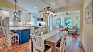 A modern kitchen with a central island, white cabinetry, and a dining area with a wooden table and chairs.
