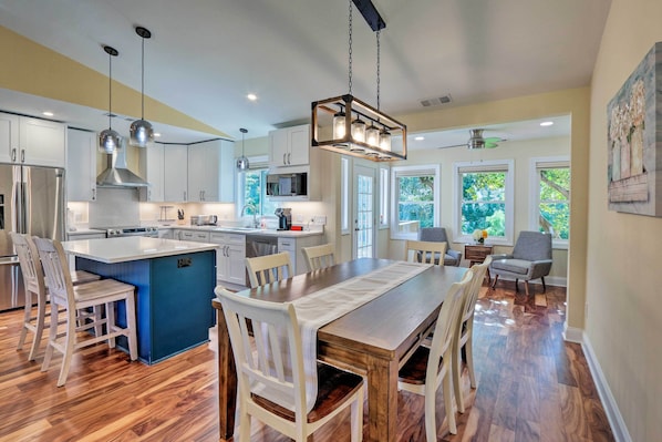 Una cocina moderna con una isla central, armarios blancos y un comedor con mesa y sillas de madera.