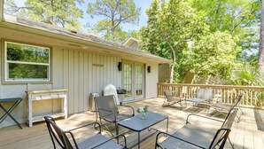 A covered outdoor patio with metal chairs and a table, a grill, and a view of the surrounding trees.
