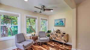 A room with hardwood flooring, two grey armchairs, a wooden sideboard, and a ceiling fan.