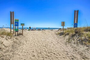 A sandy beach path with directional signs and beachgoers in the distance.
