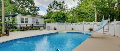 Una piscina rectangular con plataforma blanca, una escalera de metal y una cerca blanca con parte superior tipo celosía.
