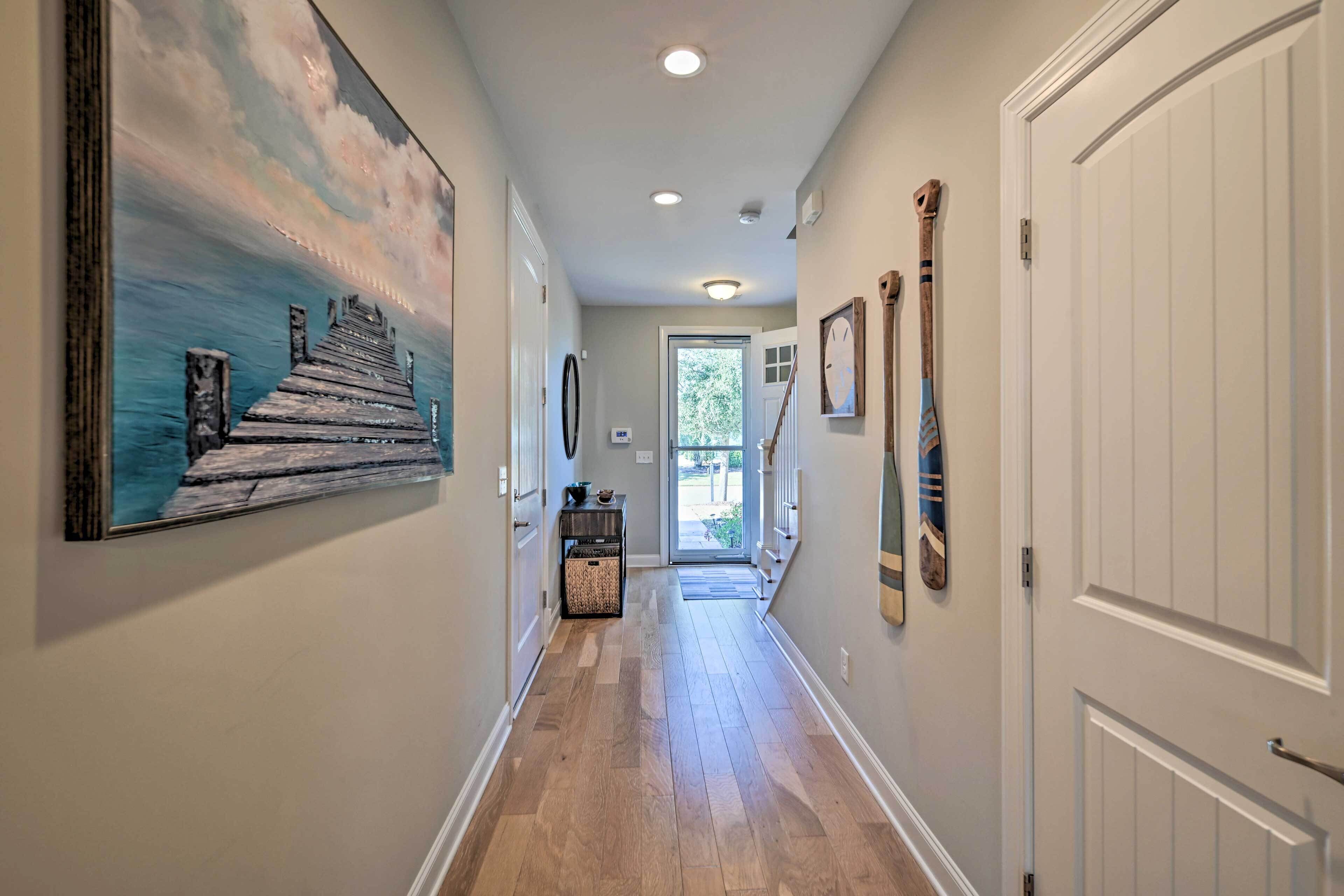 A hallway with wooden flooring, a painting of a pier, and a door with a coat hanging on it.