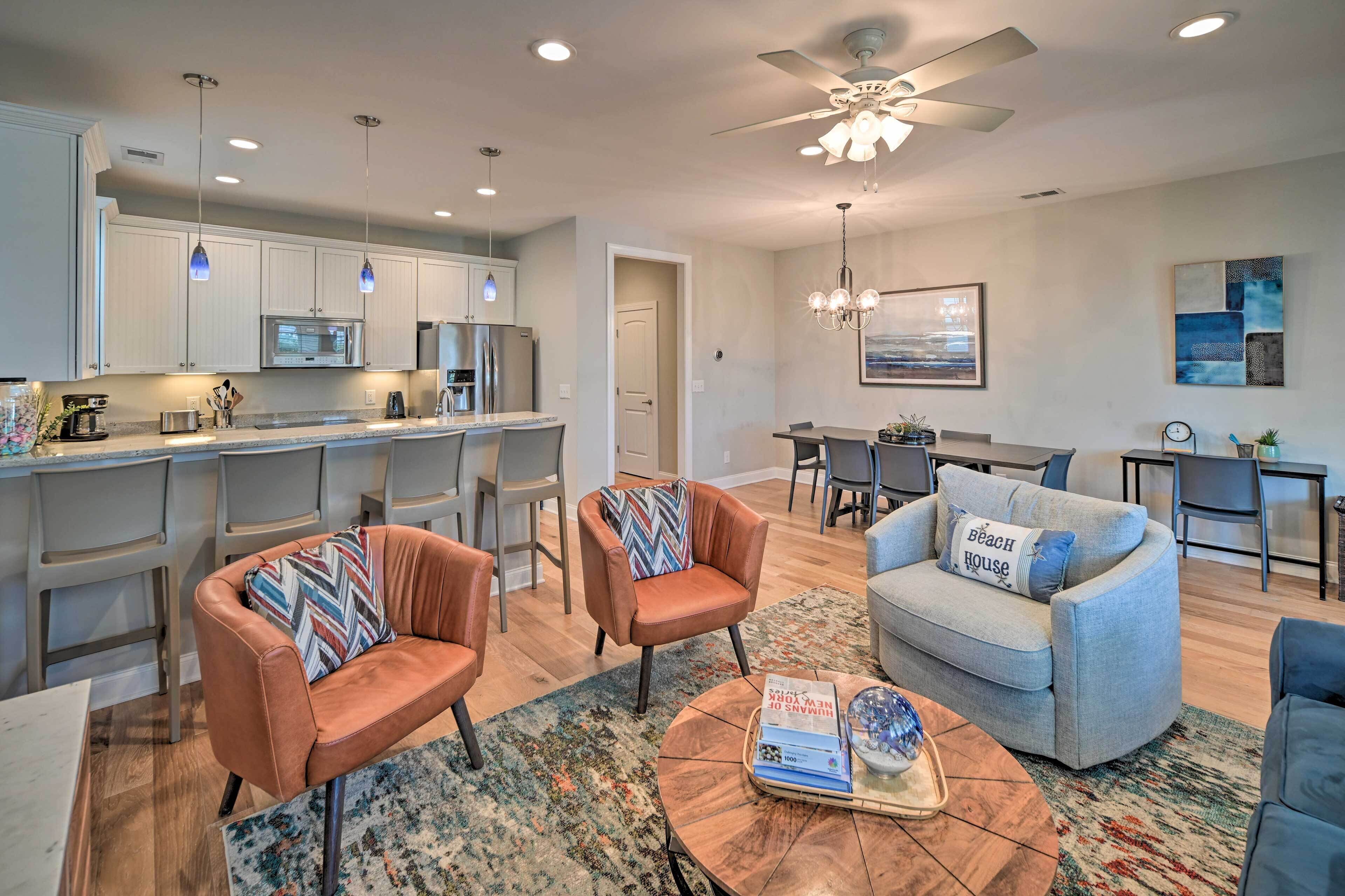 A modern kitchen with stainless steel appliances, a dining area with a round table, and a living room with a sofa and armchairs.