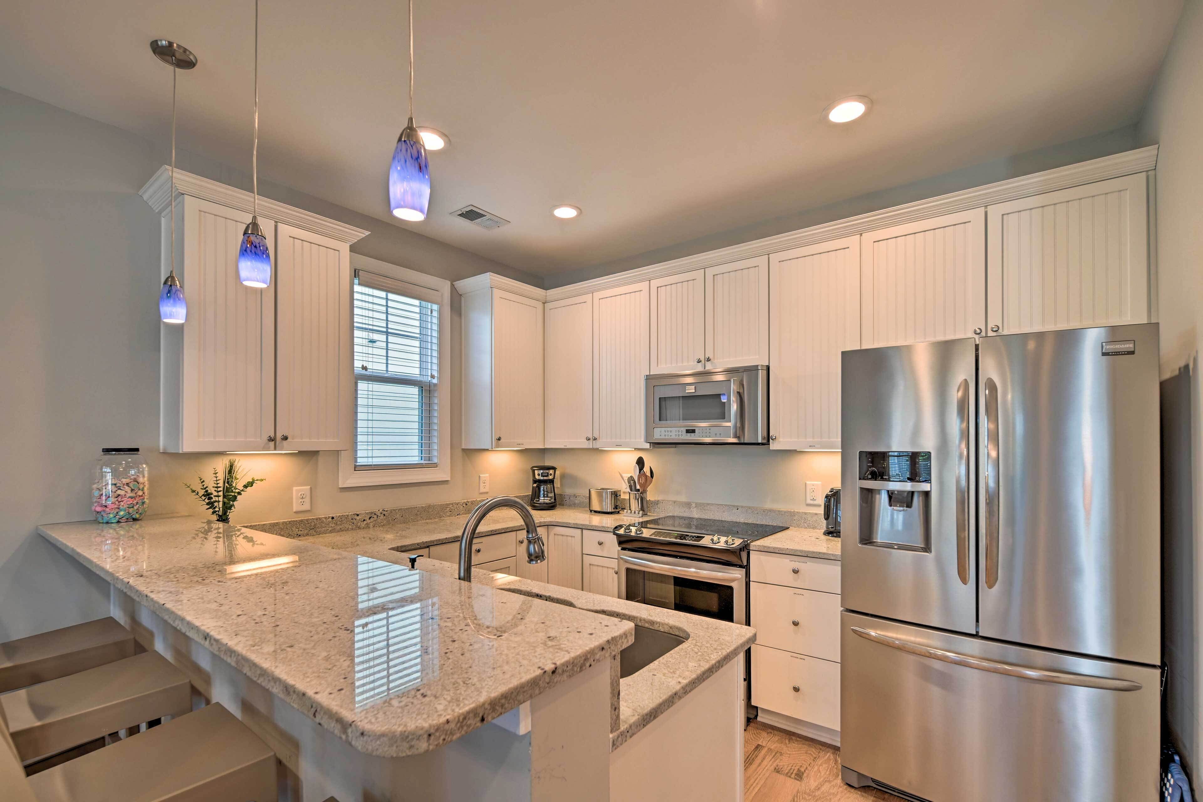 A modern kitchen with white cabinets, stainless steel appliances, granite countertops, and pendant lighting.