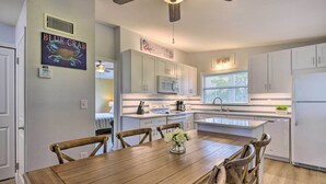 A modern kitchen with white cabinets, a wooden dining table, and a ceiling fan. - 'sarasota Sunset House' w/ Spacious Patio! (Sarasota)